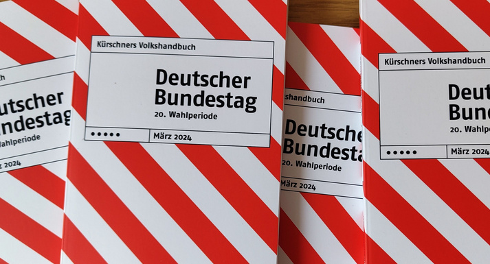 Mehrere nebeneinander liegende Exemplare des rot-weiß gestreiften Taschenbuchs "Kürschners Volkshandbuch Deutscher Bundestag".