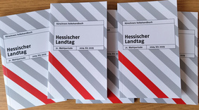 Mehrere nebeneinander liegende Exemplare des grau-weiß-rot gestreiften Taschenbuchs "Kürschners Volkshandbuch Hessischer Landtag".