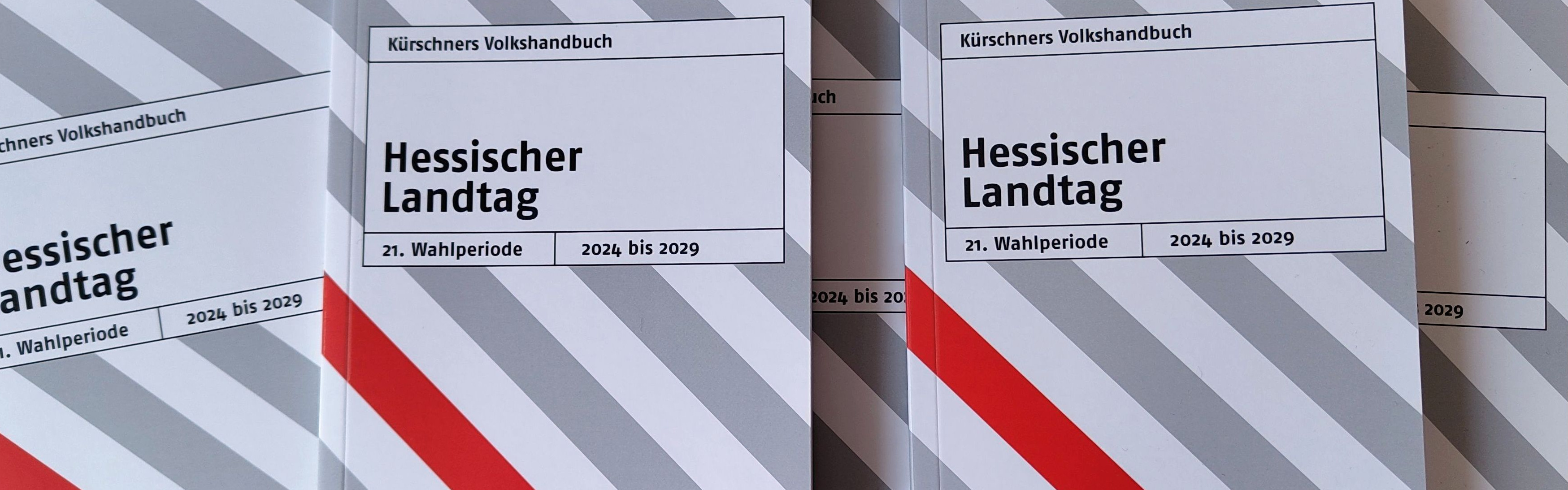 Mehrere nebeneinander liegende Exemplare des grau-weiß-rot gestreiften Taschenbuchs "Kürschners Volkshandbuch Hessischer Landtag". 